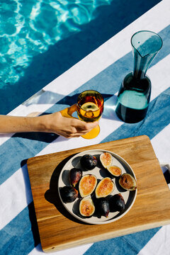 Unknown hand holding a glass ext to a bowl of figs in a pool