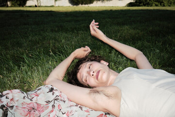 Person relaxing on the grass with floral blanket in a sunny park