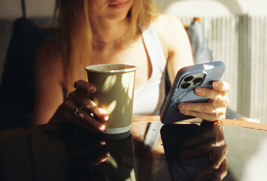 Woman drinking coffee and using smartphone