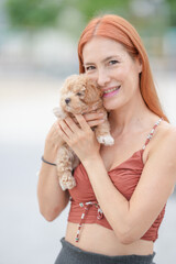 A woman is holding a small dog in her arms. The dog is brown and white. The woman is smiling and she is happy
