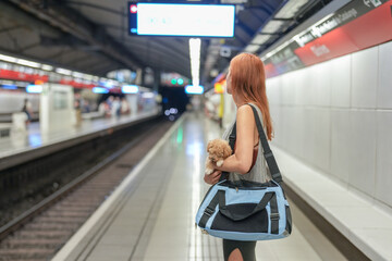 A woman is walking with a small dog in a blue bag. She is at a train station