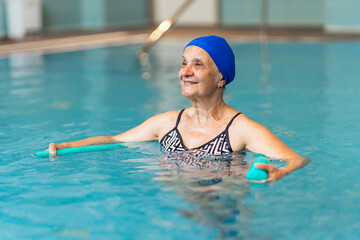 Senior woman doing aqua aerobics with foam dumbbells in swimming pool
