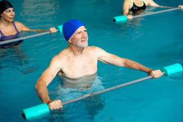 Senior man doing water aerobics with foam dumbbells in swimming pool