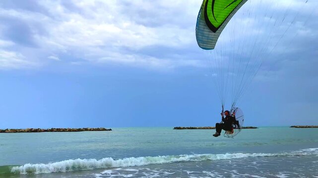 PORTO SAN GIORGIO, ITALY - SEPTEMBER 20, 2023: Paraglider in Porto San Giorgio. A sweeping, pan left view of a powered paraglider cruising low over Porto San Giorgio&rsquo;s serene Adriatic Sea shores