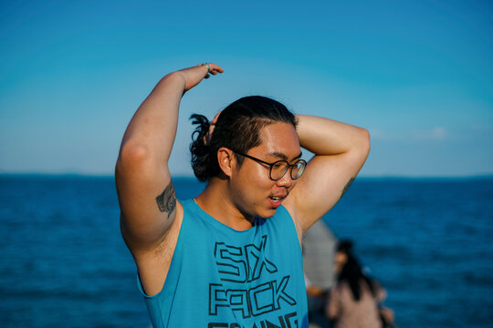 Young Man tying his hair during sunset by the sea