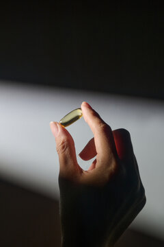 A person's hand holds a single omega-3 capsule