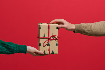 Hands Exchanging Christmas Gift Against Red Background