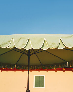 Green Patio Umbrella Against a Clear Blue Sky and Peach Wall