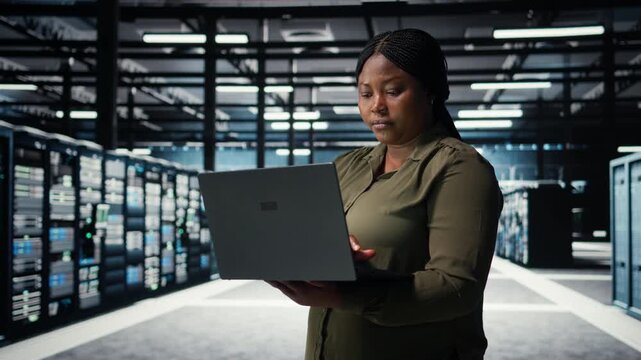 Data center system administrator using laptop to ensure error free rigs networks for intense computational demands. IT specialist uses notebook to monitor server hub gear parts for failures, camera A