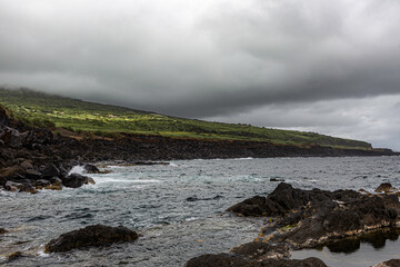 Faial, Azores, island, Portugal, Rocky shoreline with a cloudy sky in the background. The water is choppy and the rocks are scattered along the shore