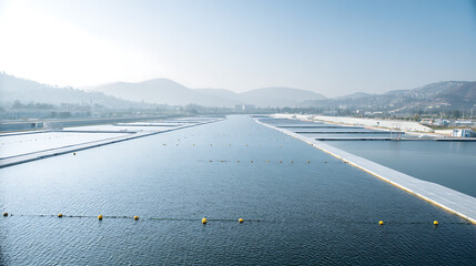 Large-scale water treatment facility with rectangular basins and surrounding mountains under clear sky