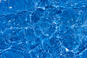 Blue water with ripples on the surface. Defocus blurred transparent blue colored clear calm water surface texture with splashes and bubbles. Water waves with shining pattern texture background.