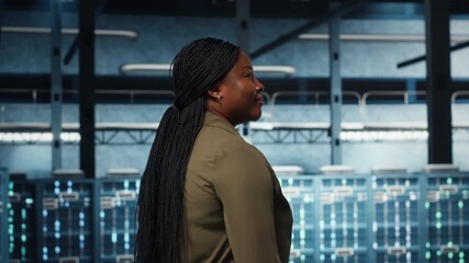 Data center technician conducts security audits to protect against cyber threats and malfunctions. African american woman walking in server room, ensuring compliance with industry standards, camera B - Powered by Adobe