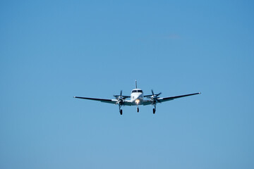 Small propeller plane flying in the blue sky on a sunny day. Twin-engine plane soaring through a clear blue sky.