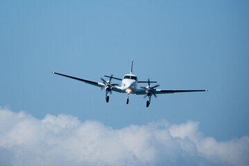 Twin-engine plane in the sky against the clouds. A propeller plane approaches the runway against a...