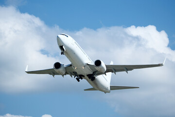 White plane climbing higher against the clouds. Airplane flying in the blue sky, take-off from airport