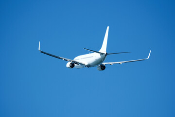 The plane that's just taken off drifts away from the airport across clear blue sky. Airplane flying in the blue sky on a sunny day. Airplane taking off, rear view. Travel concept.