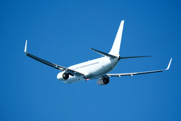 The plane that's just taken off drifts away from the airport across clear blue sky. Airplane flying in the blue sky on a sunny day. Airplane taking off, rear view. Travel concept.