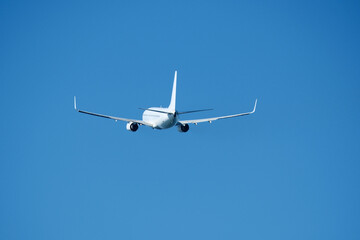 The plane that's just taken off drifts away from the airport across clear blue sky. Airplane flying in the blue sky on a sunny day. Airplane taking off, rear view. Travel concept.
