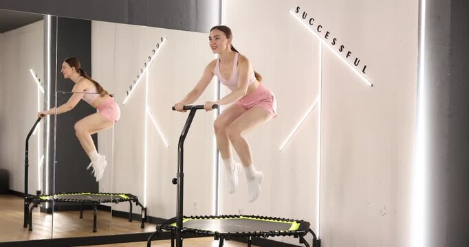Smiling woman jumping on mini exercise trampoline near mirror in fitness studio