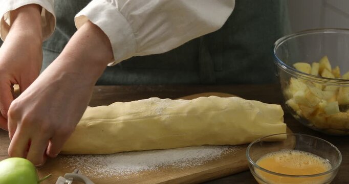 Woman making delicious apple strudel at wooden table in kitchen, closeup