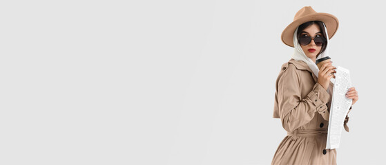 Fototapeta premium Female spy with newspaper and coffee cup on light background