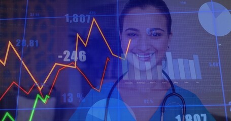 Smiling Indian nurse in blue scrubs and stethoscope analyzing financial data in studio, with charts