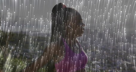 Standing Black runner wearing purple sports bra and white earphones on hillside, with rain streaks