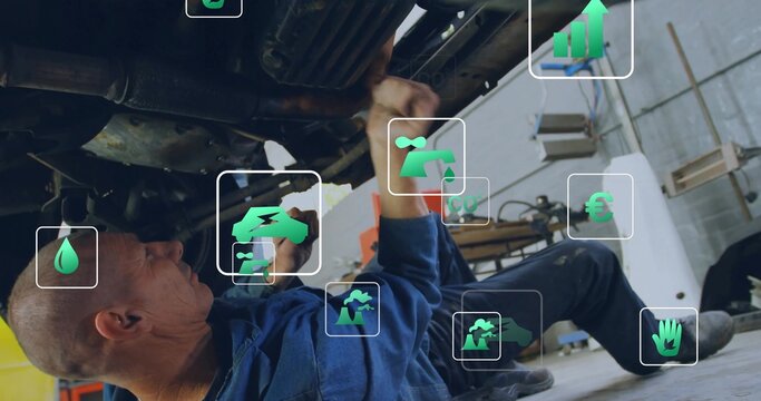 Fototapeta Wrenching mechanic wearing blue coverall addressing car undercarriage in workshop, with green icons
