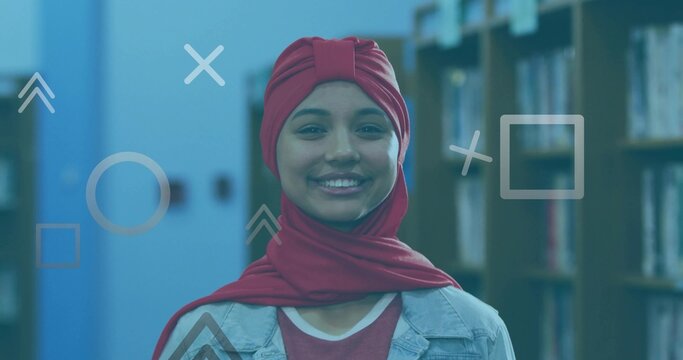 Smiling student wearing red turban headscarf and denim jacket in library aisle with floating shapes - Powered by Adobe