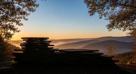 Gray stone slab with round top on mossy cliff edge. Overlooks valley with lush green vegetation, mountains shrouded in dense fog. Natural landscape, serene atmosphere, perfect for product placement.