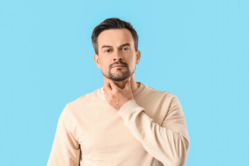 Handsome man self-examining thyroid gland on blue background