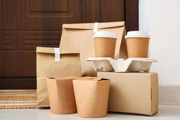 Paper bags with coffee cups on mat near door, closeup. Food delivery service
