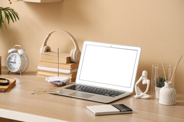 Inventor's workplace with blank laptop and books near beige wall in office