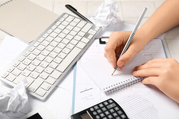 Young woman working with keyboard, schematics and crumpled paper at table, closeup. Inventor concept
