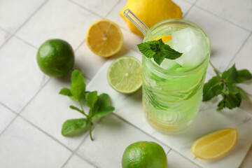 Glass of tasty cold cocktail and citrus fruits on white tile background, closeup