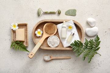 Wooden tray with towel, facial massage tools and bottles of cosmetic products on white grunge background
