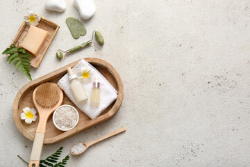 Wooden tray with towel, facial massage tools and bottles of cosmetic products on white grunge background