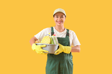 Female janitor with cleaning supplies on yellow background