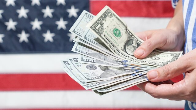 American Dream Hands Holding US Currency Against Backdrop of the American Flag. Finance