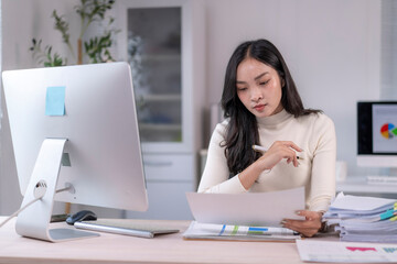 Asian businesswoman analyzing marketing data using computer and documents at office
