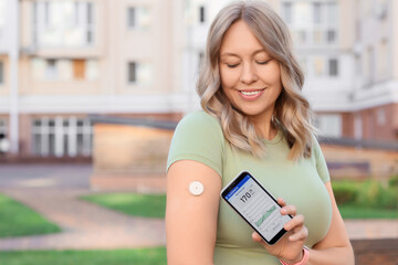 Diabetic woman with glucose sensor using mobile phone for measuring blood sugar level outdoors
