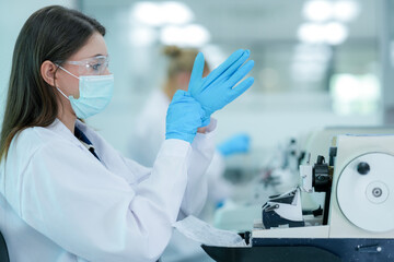 A histotechnologist dons sterile nitrile gloves, following aseptic technique and safety protocols before operating a microtome to section tissue specimens in a pathology laboratory.