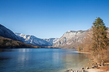 Wide panorama of Lake Bohinj, bohinjsko Jezero, in Slovenia with snow-dusted Julian Alps mounts, depicting the alpine lake inside Triglav National Park from a peaceful shoreline viewpoint.