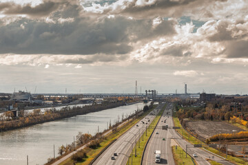 Obraz premium Aerial view of Longueuil on Montreal South Shore shows a wide expressway running beside the St Lawrence in Canada. Traffic, bridges, power lines and industrial sites describe a North American drive.