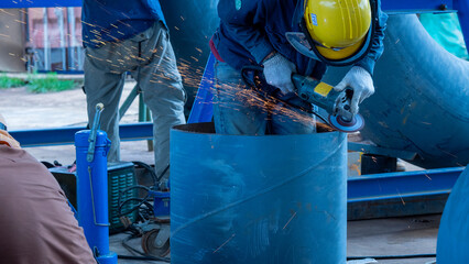 In a busy workshop, a worker wearing a helmet and gloves uses an angle grinder to cut through a...