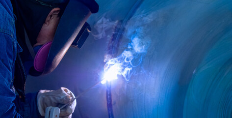 A skilled worker is performing welding in an industrial environment. Sparks and smoke are visible...