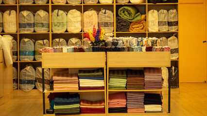 Shelves filled with neatly arranged towels, blankets, and bedding create a welcoming shopping environment. A table in front showcases soft fabrics in various colors, inviting customers to explore