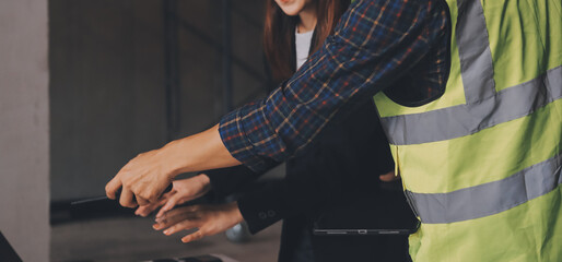 Construction manager and engineer dressed in orange work vests and hard helmets explore...