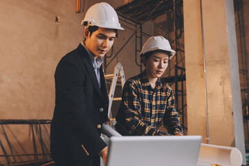 Construction manager and engineer dressed in orange work vests and hard helmets explore construction documentation on the building site near the steel frames